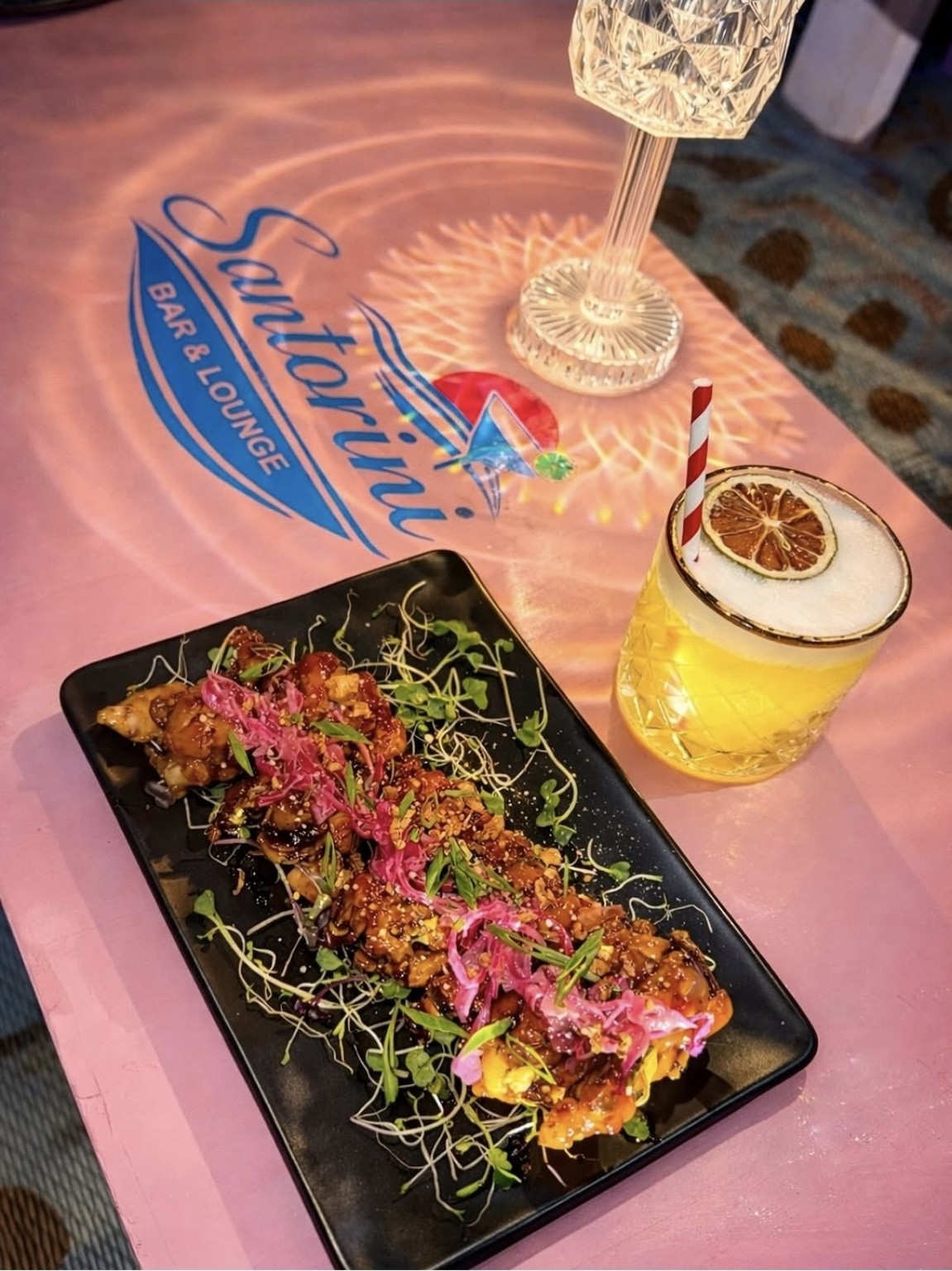 Glazed bites and a yellow cocktail on a pink Santorini table